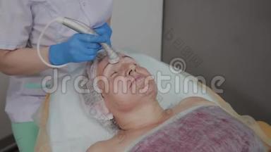 专业美容师在美容办公室为一名携带微电流的老年妇女执行手术。